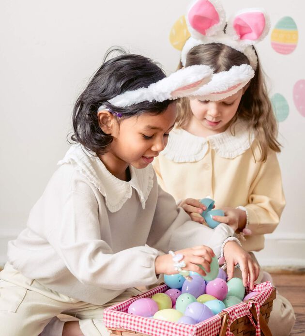 Curious girls choosing Easter eggs placed in wicker basket